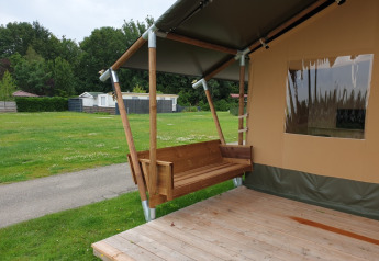 Safari telt med toilet ved Camping Gorishoek i Holland, viser en træveranda og gyngebænk udenfor.