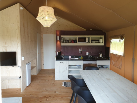 Vista interior de tienda Safari con muebles de madera, cocina pequeña y lámpara colgante en Camping Gorishoek.