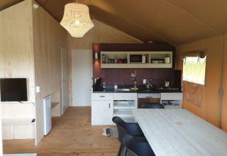 Vista interior de tienda Safari con muebles de madera, cocina pequeña y lámpara colgante en Camping Gorishoek.