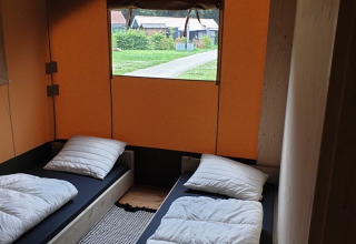 To enkeltsenge i et safari telt med orange vægge på Camping Gorishoek i Holland, udsigt gennem vinduet.