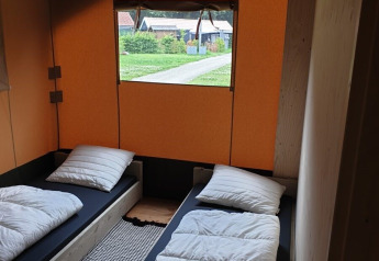To enkeltsenge i et safari telt med orange vægge på Camping Gorishoek i Holland, udsigt gennem vinduet.