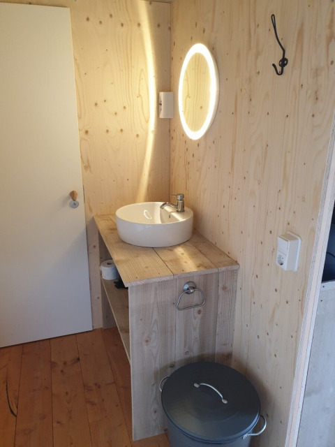 Baño con paredes de madera, lavabo redondo, espejo iluminado y cubo en tienda safari en Países Bajos.