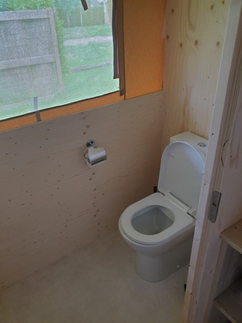 Bagno con wc in una tenda safari con pareti di legno e ampia finestra, Camping Gorishoek, Paesi Bassi.