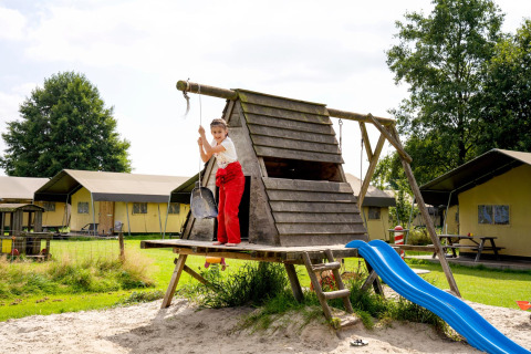 Niño jugando en un parque infantil en FarmCamps t Looveld, un parque vacacional en Drenthe, Países Bajos, con tiendas detrás.
