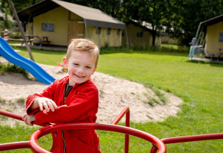 Jongen in rode jas speelt vrolijk op speelplein bij FarmCamps t Looveld, Drenthe, Nederland, buitenlucht.