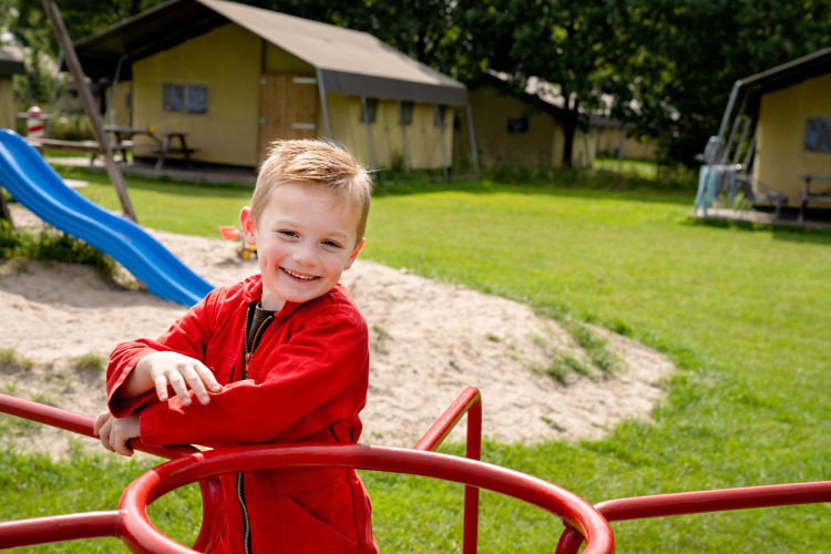 Lachende jongen in rode jas speelt op speeltoestel bij FarmCamps t Looveld in Drenthe, Nederland, buiten.