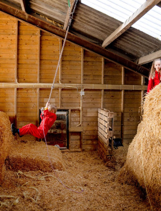 Niños juegan sobre pacas de heno y una cuerda en el granero de FarmCamps t Looveld en Drenthe, Países Bajos.