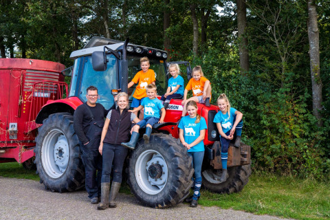 Familia sonriente junto a un tractor rojo en FarmCamps t Looveld, parque vacacional en Drenthe, Países Bajos.
