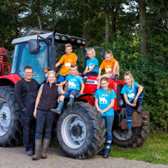 Familia sonriente junto a un tractor rojo en FarmCamps t Looveld, parque vacacional en Drenthe, Países Bajos.