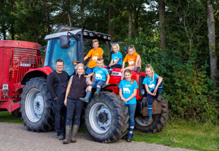 Famille souriante devant un tracteur rouge à FarmCamps t Looveld, parc de vacances à Drenthe, Pays-Bas.