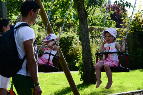 Niñas en columpios y adultos en Camping Troisvierges, parque vacacional en Clervaux, Luxemburgo.