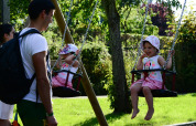 Bambini sorridenti sulle altalene al Camping Troisvierges, parco vacanze in Lussemburgo.