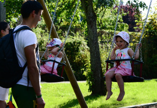 Niñas en columpios y adultos en Camping Troisvierges, parque vacacional en Clervaux, Luxemburgo.