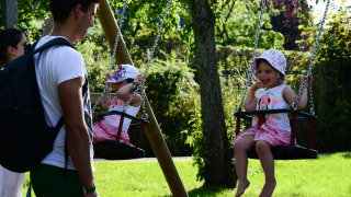 Niñas en columpios y adultos en Camping Troisvierges, parque vacacional en Clervaux, Luxemburgo.