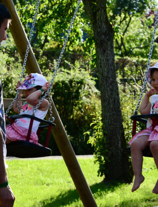 Niñas en columpios y adultos en Camping Troisvierges, parque vacacional en Clervaux, Luxemburgo.