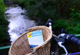 Panier de vélo avec une carte Vennbahn au bord d'une rivière, Camping Troisvierges, Canton de Clervaux, Luxembourg.