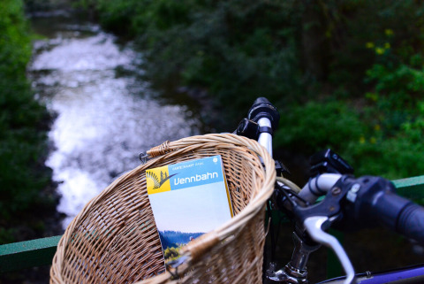 Panier de vélo avec une carte Vennbahn au bord d'une rivière, Camping Troisvierges, Canton de Clervaux, Luxembourg.