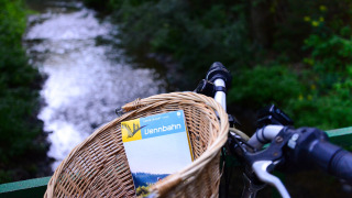 Cesta de bicicleta con un mapa de Vennbahn junto a un río en Camping Troisvierges, Cantón Clervaux, Luxemburgo.