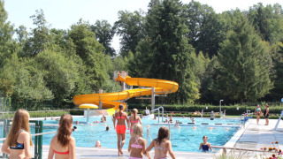 Niños y adultos disfrutan de la piscina al aire libre y tobogán amarillo en Camping Troisvierges, Luxemburgo.