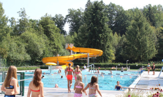 Niños y adultos disfrutan de la piscina al aire libre y tobogán amarillo en Camping Troisvierges, Luxemburgo.