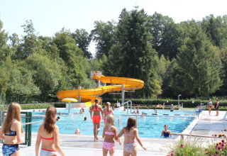 Kinderen en volwassenen genieten van het zwembad en de gele glijbaan op Camping Troisvierges, Luxemburg.