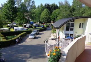 Blick auf Camping Troisvierges in Luxemburg mit Wohnwagen, grünen Hecken und modernem Gebäude.