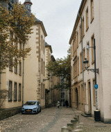 Calle adoquinada y estrecha en Troisvierges, Luxemburgo, bordeada de edificios antiguos y un auto aparcado.