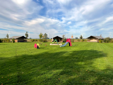 Safari tent at Boerderijcamping de Hinde in the Netherlands with playground and wind turbines behind.