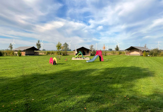 Safari tent at Boerderijcamping de Hinde in the Netherlands with playground and wind turbines behind.