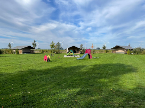Safari-Zelt bei Boerderijcamping de Hinde in den Niederlanden mit Spielplatz und Windrädern im Hintergrund.