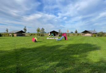 Safari-Zelt bei Boerderijcamping de Hinde in den Niederlanden mit Spielplatz und Windrädern im Hintergrund.