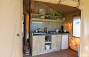 Et veludstyret køkkenområde i et glamping-telt med træskabe, gaskomfur, køleskab og vindue.