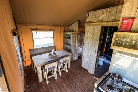 Interior of a stylish glamping tent featuring a wooden dining table, kitchenette, and bunk beds.