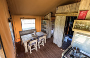 Interno di una tenda glamping moderna con tavolo da pranzo in legno, letti a castello e cucina.