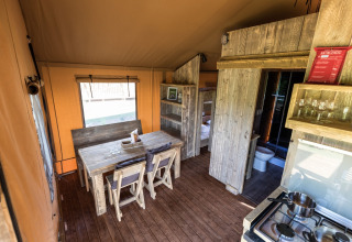 Intérieur d'une tente de glamping avec table en bois, kitchenette, lits superposés et toilettes.