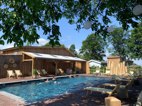 Piscina al aire libre con tumbonas y refugios de madera en Camping Mareveld, parque vacacional en Limburg, Países Bajos.