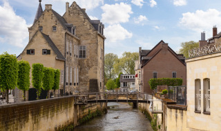 Edificios históricos y un pequeño río en Schimmert, Limburg, Países Bajos, bajo un cielo azul con nubes.