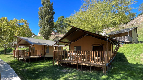 Tiendas safari con terraza de madera y baños en Camping l'Ardechois, Francia, rodeadas de naturaleza.