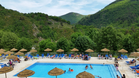 Camping l'Ardechois en Auvergne-Rhône-Alpes, Francia, con piscina al aire libre, tumbonas y montañas verdes.