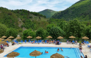 Camping l'Ardechois en Auvergne-Rhône-Alpes, Francia, con piscina al aire libre, tumbonas y montañas verdes.