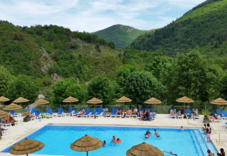 Camping l'Ardechois in Auvergne-Rhône-Alpes, Frankreich, mit Pool, Sonnenliegen und grünen Bergen im Hintergrund.