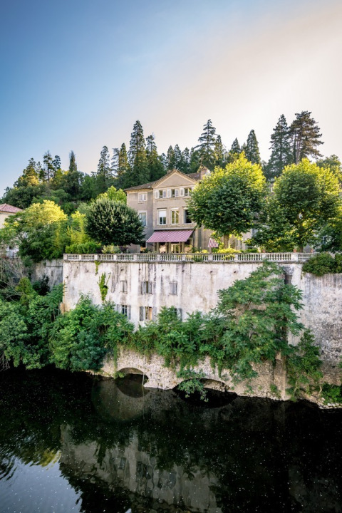 Elegant holiday park in Auvergne-Rhône-Alpes, France, featuring a villa by the river and lush trees.