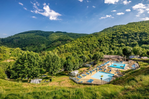 Campsite with swimming pools nestled among green hills and forests in Auvergne-Rhône-Alpes, France.