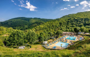 Campingplads med swimmingpools omgivet af grønne bakker og skov i Auvergne-Rhône-Alpes, Frankrig.