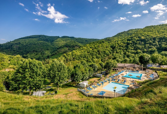 Campingplads med swimmingpools omgivet af grønne bakker og skov i Auvergne-Rhône-Alpes, Frankrig.
