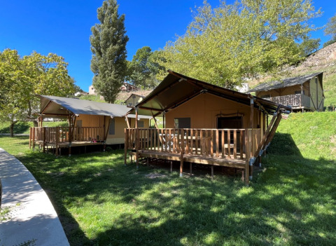 View of luxury safari tents on wooden decks at Camping l'Ardechois, Auvergne-Rhône-Alpes, France, in sunlight.