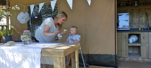 Moeder en kind genieten van glamping op een vakantiepark, met gezellige aankleding en buitentafel.
