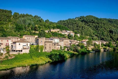 Photo of Camping l'Ardechois, a holiday park by the riverside with green hills in Auvergne-Rhône-Alpes, France.