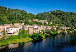 Photo of Camping l'Ardechois, a holiday park by the riverside with green hills in Auvergne-Rhône-Alpes, France.