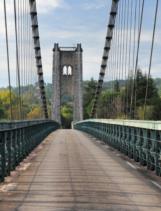 A scenic suspension bridge near Gluiras in Auvergne-Rhône-Alpes, France, surrounded by lush greenery.